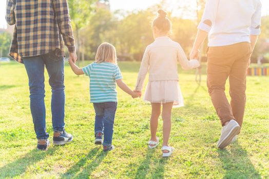 Rear view of two children walking hand in hand with their dads in the park in a sunny day