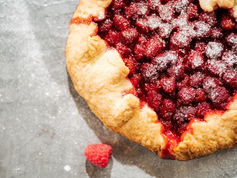 Perfect raspberry galette. Delicious rustic homemade tart with frozen or fresh raspberries on gray textured background. Beautiful round shape galette with raspberries,copy space. Top view or flat lay