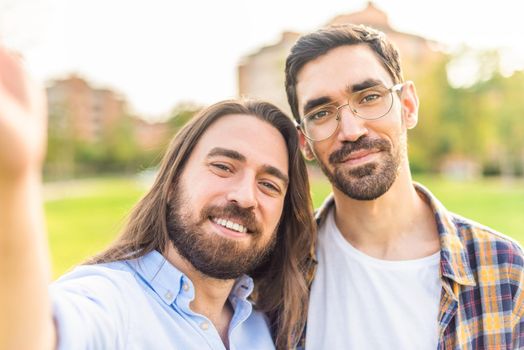 Front view of a happy gay couple taking a selfie in the park in a sunny day