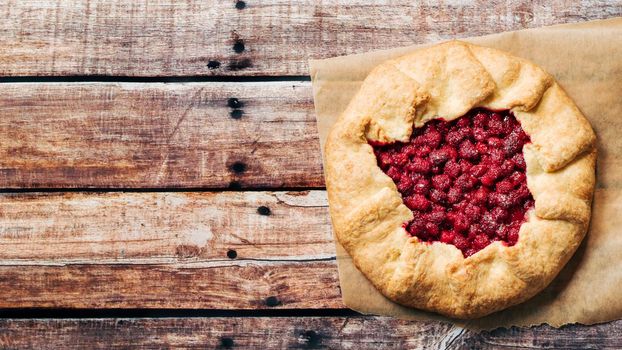 Perfect raspberry galette. Delicious rustic homemade tart with frozen or fresh raspberries on old wooden background. Beautiful round shape galette with raspberries,copy space. Top view or flat lay