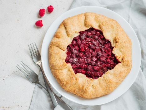Perfect raspberry galette. Delicious rustic homemade tart with frozen or fresh raspberries on white textured background. Beautiful round shape galette with raspberries,copy space. Top view or flat lay