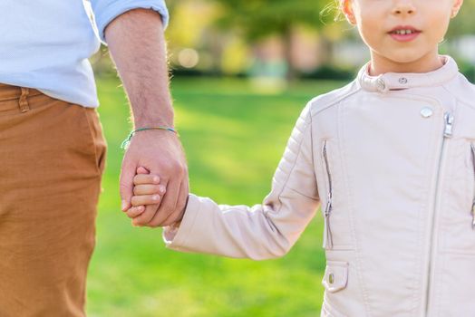 Close-up view of the holding hands of the daughter and unrecognizable father in the park