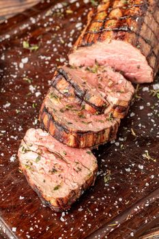 Sliced grilled beef tenderloin seasoned with salt, rosemary and thyme on a wooden cutting board