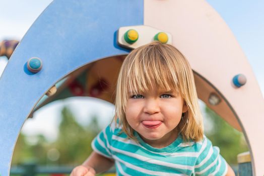 Portrait of a naughty little boy looking at camera sticking his tongue out in the playground.