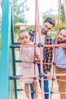Vertical image of a little girl in the playground with her two parents looking at the camera unhappy. First days after adoption, she has a hard time adjusting.