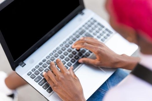 Close up top view of the hands of an african woman using a laptop int he street