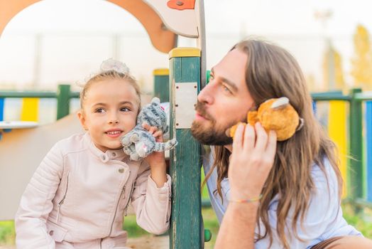 Portrait of a little girl and her father playing with stuffed animals using them as phones.