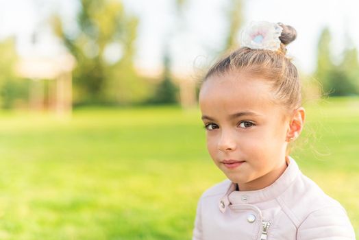 Portrait of a little girl sitting on grass in a park looking at camera with copy space and a blurred background