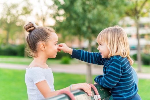 Side view of a little brother grabbing nose of little sister at park.