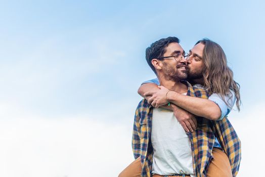 Front view of a young man carrying his partner on his back while kissing on cheek with copy space