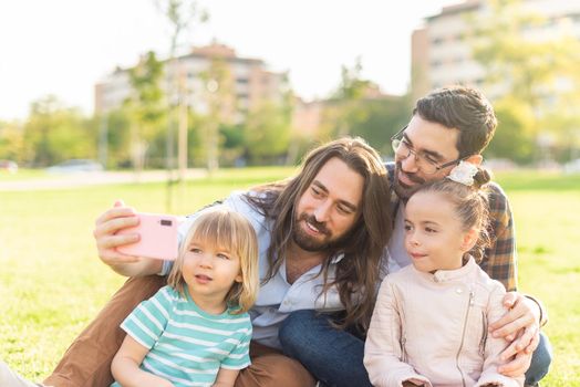 Portrait of a young gay male couple with their children taking a selfie in the park in a sunny day