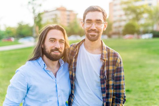 Portrait of a happy gay couple looking at camera spending time together in the park in a sunny day