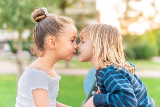 Side view of children pressed their noses to each other and looking into his eyes and smile in a park.