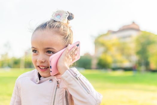 Close up of a little girl talking on smart phone in the park with copy space.