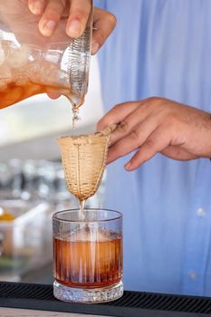 Professional bartender pouring cocktail into glass glass with shaker