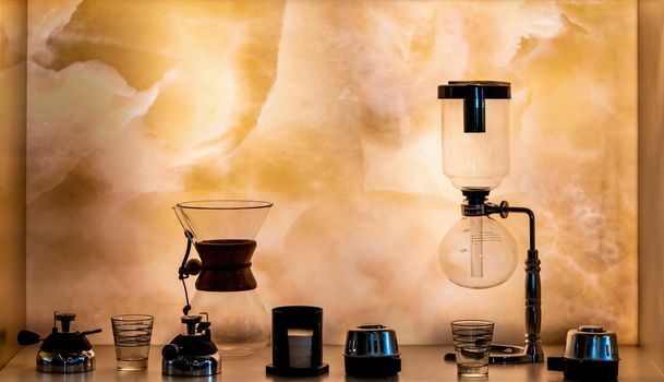 Alternative third generation coffee brewing equipments standing on the illuminated shelf. Selective focus