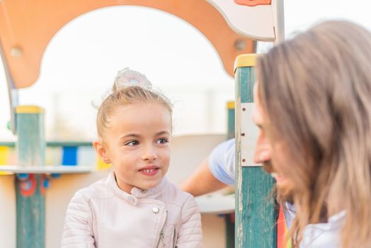 Front view of a little daughter smiling and looking to her young dad in the playground