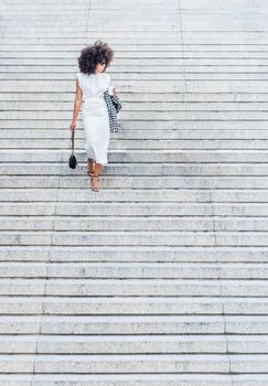 black woman alone walking down the stairs looking to the side in a white dress