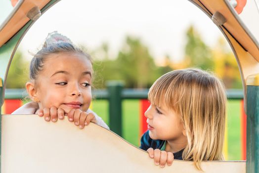 Portrait of a little sister and brother leaning with their hands and chin on a playground set looking at each other