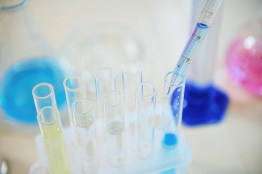 Selective focus on a dripping reagent from a glass laboratory pipette into a test tube with blue chemical liquid substance in a scientific research laboratory. Science, medicine and pharmacology