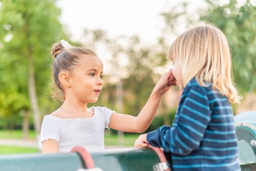 Side view of a little sister grabbing nose of little brother at park