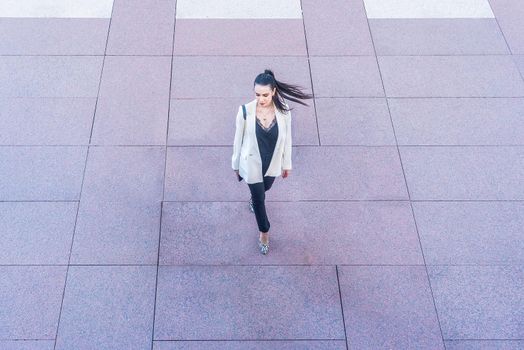 woman in white jacket walking with ponytail swinging, view from above