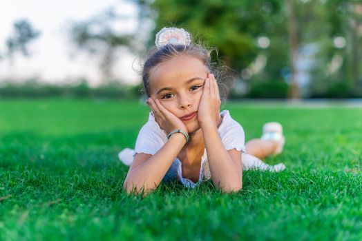 Portrait of a little girl lying on grass with her hands on her cheeks looking at camera.