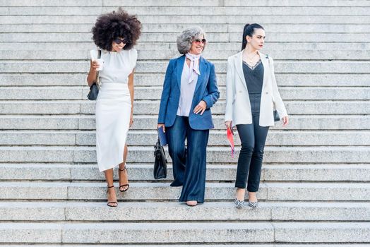 female executive workers looking to the side as they walk down the stairs in their suits