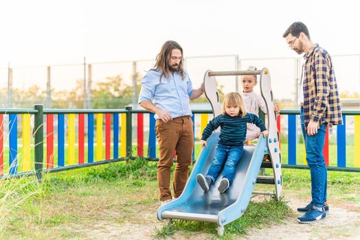 Full length view of a little boy playing on slider of playground with his family.