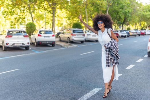 enterprising woman in a white dress hailing a taxi in the city, parked cars in the background