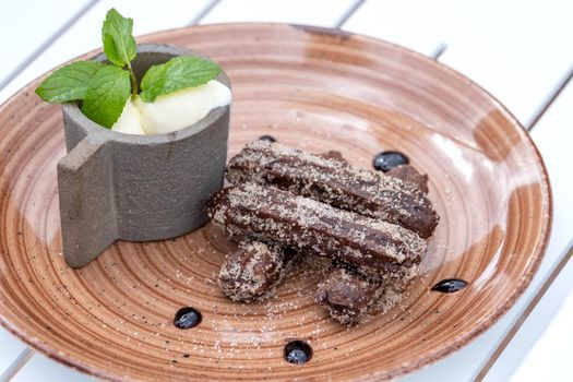 Chocolate churros with ice cream on a brown porcelain plate