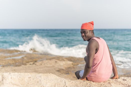 black man sitting on the sand with his head turned around looking at camera