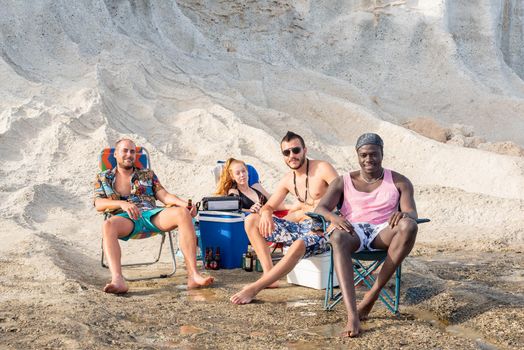 four friends sitting on the beach having a picnic with a cooler and chairs, horizontal picture