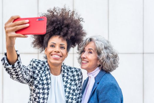 two friends at work taking a selfie with a red mobile phone, cut out view