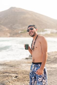 Male young adult in swimsuit posing happily with a drink on the beach, portrait, foggy background