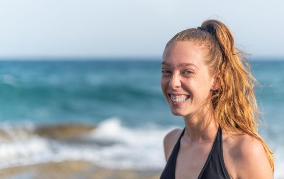 young woman looking at the camera smiling with the sea in the background, horizontal portrait