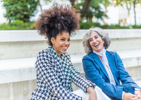 black woman with afro hair laughing looking at the camera next to laughing mature woman