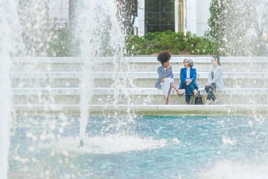 three female workers talking while sitting in front of a fountain, water falling in the foreground