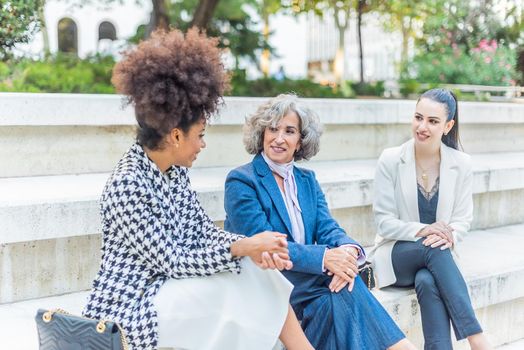 three female co-workers talking business while sitting in the street, horizontal close up