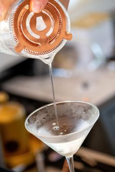 Professional bartender pouring cocktail into glass glass with shaker