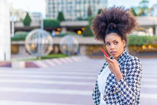 woman sending an audio message in the street with the phone near her mouth. Urban background