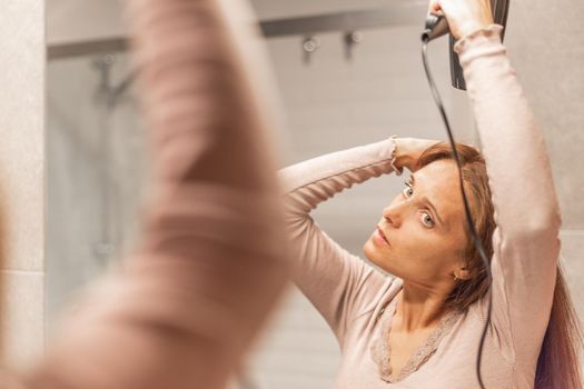 An adult woman drying her hair with a hair dryer in the bathroom of her hotel room. Concept of hotel.