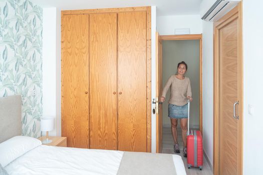 A happy adult woman entering the hotel room where she will be staying carrying her suitcase. Concept of hotel room.