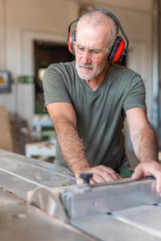 Man in safety glasses and headset working on a sliding table saw, close-up