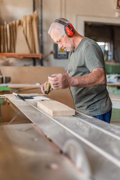 Male worker measuring a wooden step on a sliding table saw, vertical background