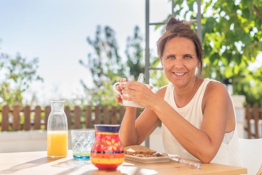 A cheerful adult woman looking at camera having breakfast with coffee, toast and orange juice in her rural house or hotel in Almeria, Spain.