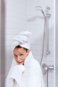 An adult caucasian woman comes out of the shower after taking a hot shower with a towel and very cold looking at the camera. Concept of hotel room.