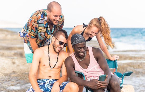 four young people on the beach looking at the photos they have taken with their phone, portrait view