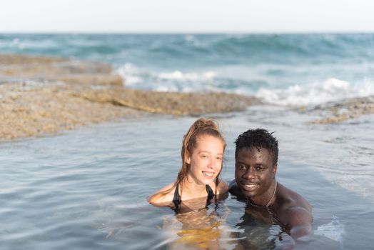 young black man and white woman bathing in the sea looking at the camera, portrait