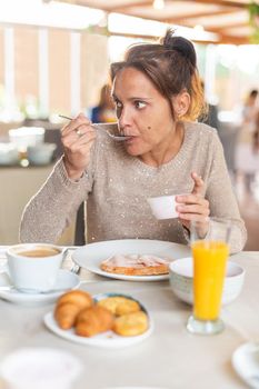 Vertical image of an adult woman having breakfast in a hotel dinning room while eat fruits with spoon in a small bowl. Concept of breakfast in hotel.